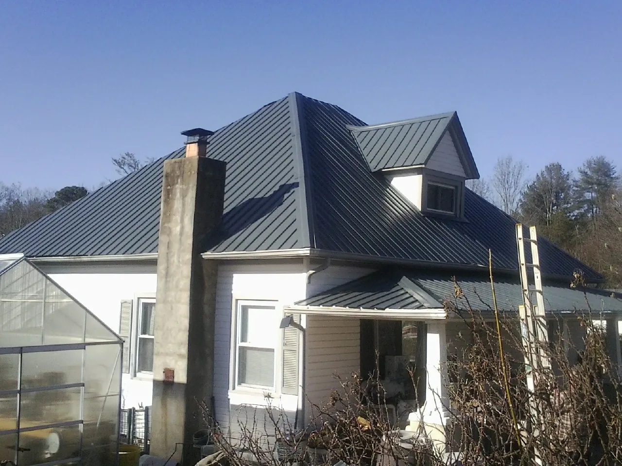 Dark blue standing seam metal roof on a white farmhouse with dormer — Slate & Tile Roof Repair by Roofing Brothers in Glenshaw