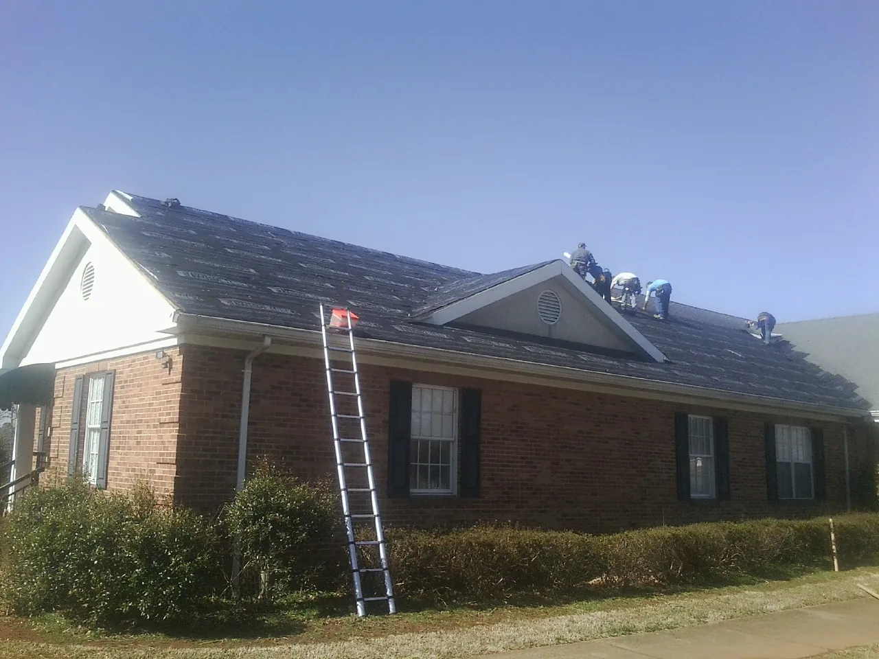 Crew tearing shingles off a brick ranch roof with a ladder set — Metal Roof Repair work by our crew in Glenshaw