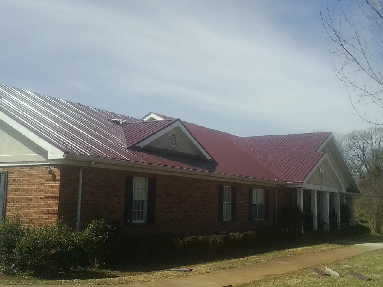 Red metal roof with gabled entries on a long brick building, from a Hail Damage Roof Repair job in Glenshaw