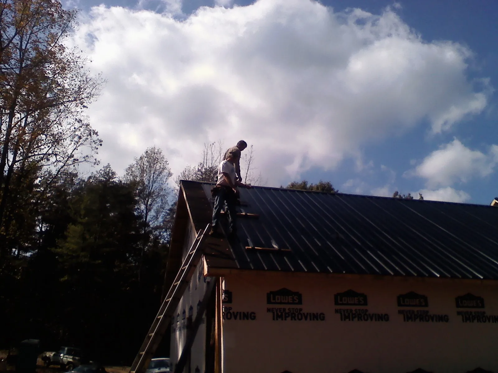 Roofer fastening dark metal panels high against a cloudy sky, from a Roof Inspection job in Glenshaw