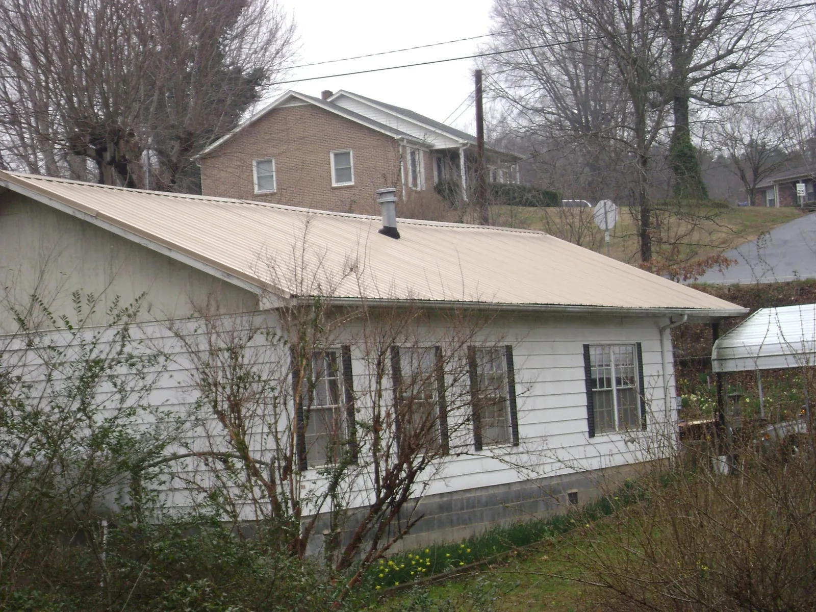 Tan metal roof on a white sided house set into a hillside — Commercial Roofing by Roofing Brothers in Glenshaw